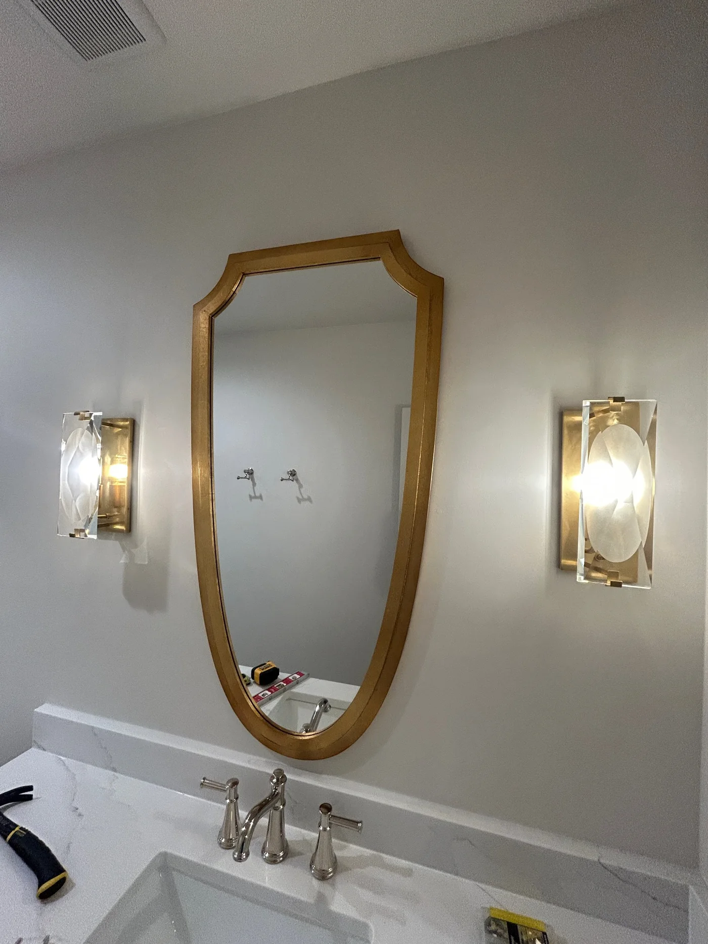 Gold shaped mirror installed between sconces