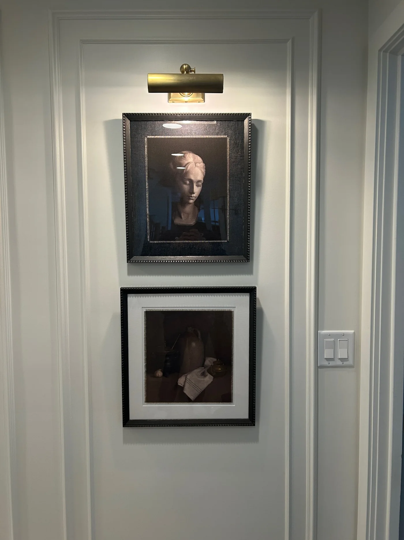 Two framed artworks aligned beneath a picture light